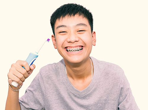 Smiling asian boy with braces holding electric toothbrush